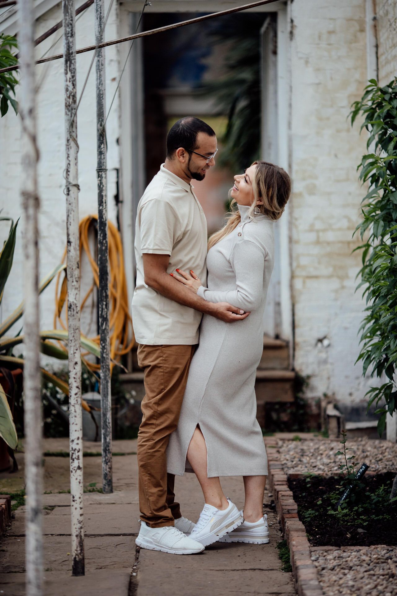 Intimate couple photoshoot against white brick wall with natural greenery.