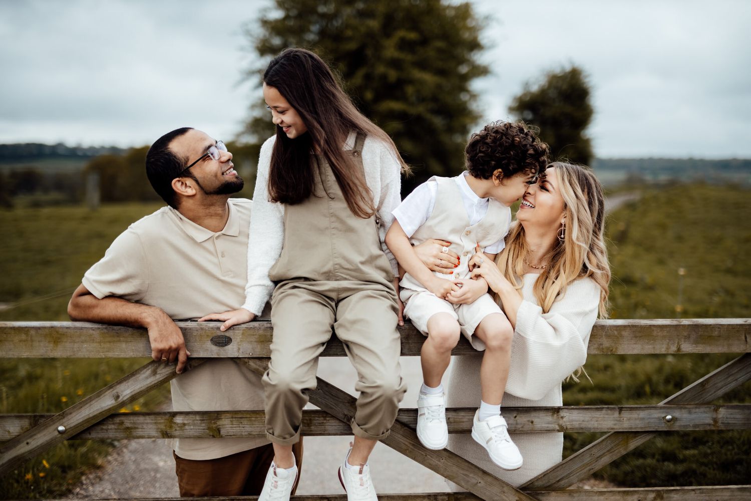 A group sits playfully on wooden logs during a countryside photoshoot in neutral-colored clothing.