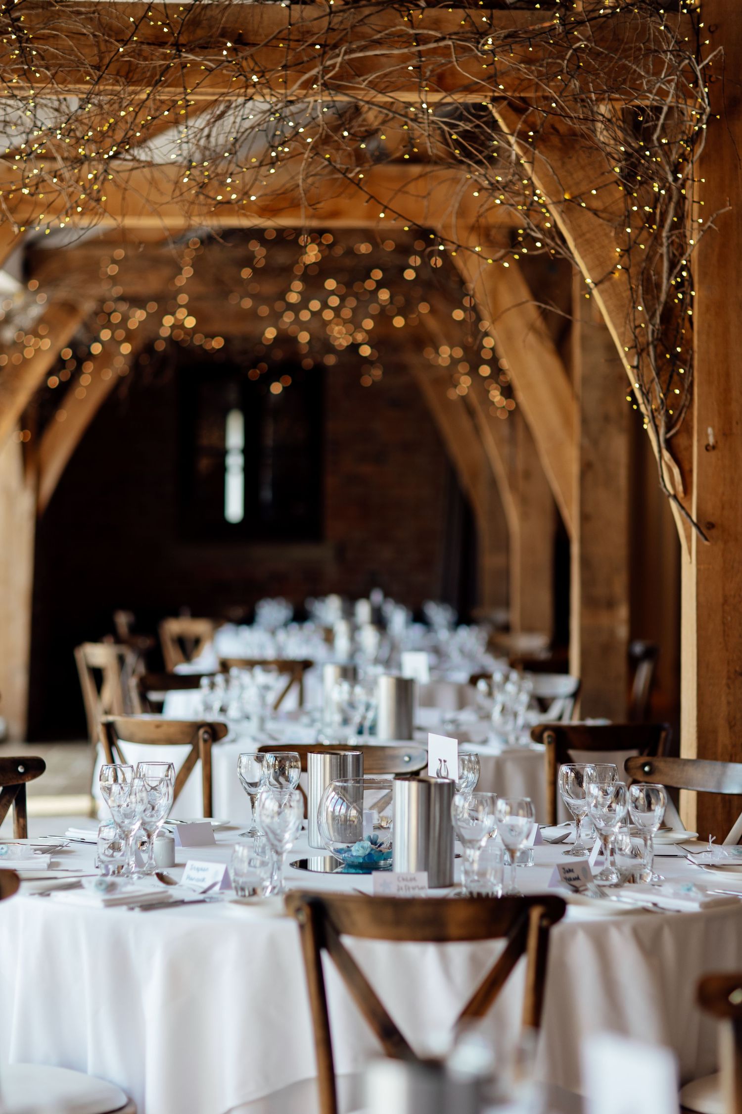 Elegant wedding reception venue with white tablecloths and twinkling lights in rustic wooden beams.