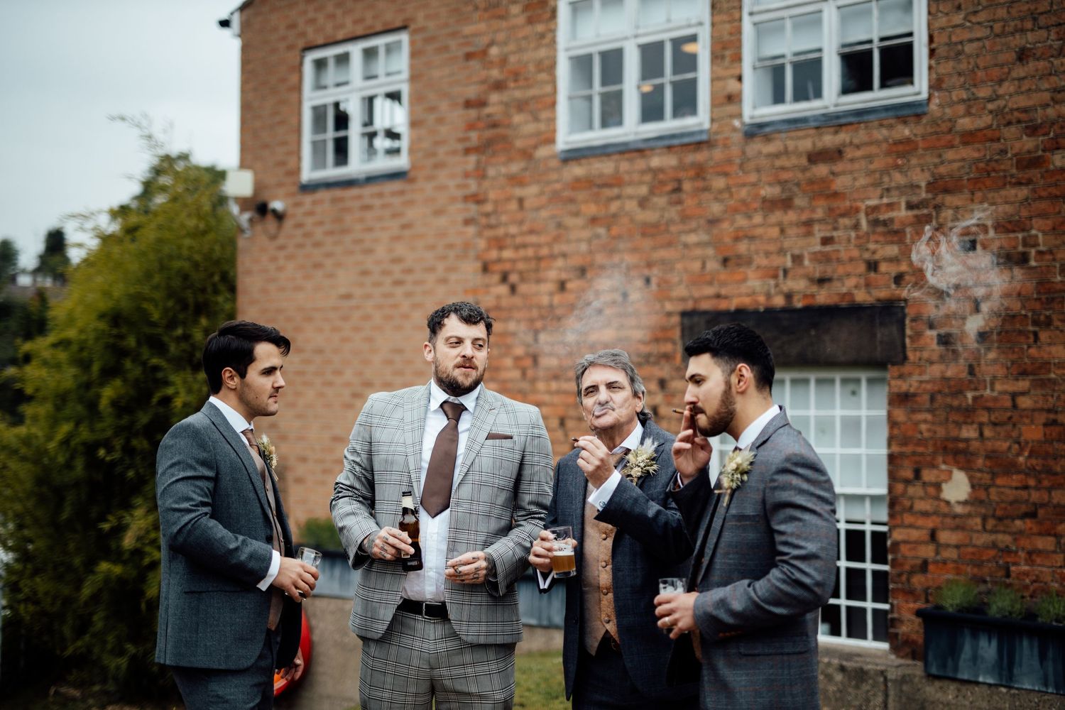 Groomsmen in gray suits socializing outside a brick building.