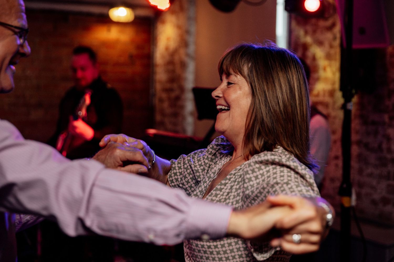 Couple dancing together in a dimly lit venue with warm lighting and brick walls.