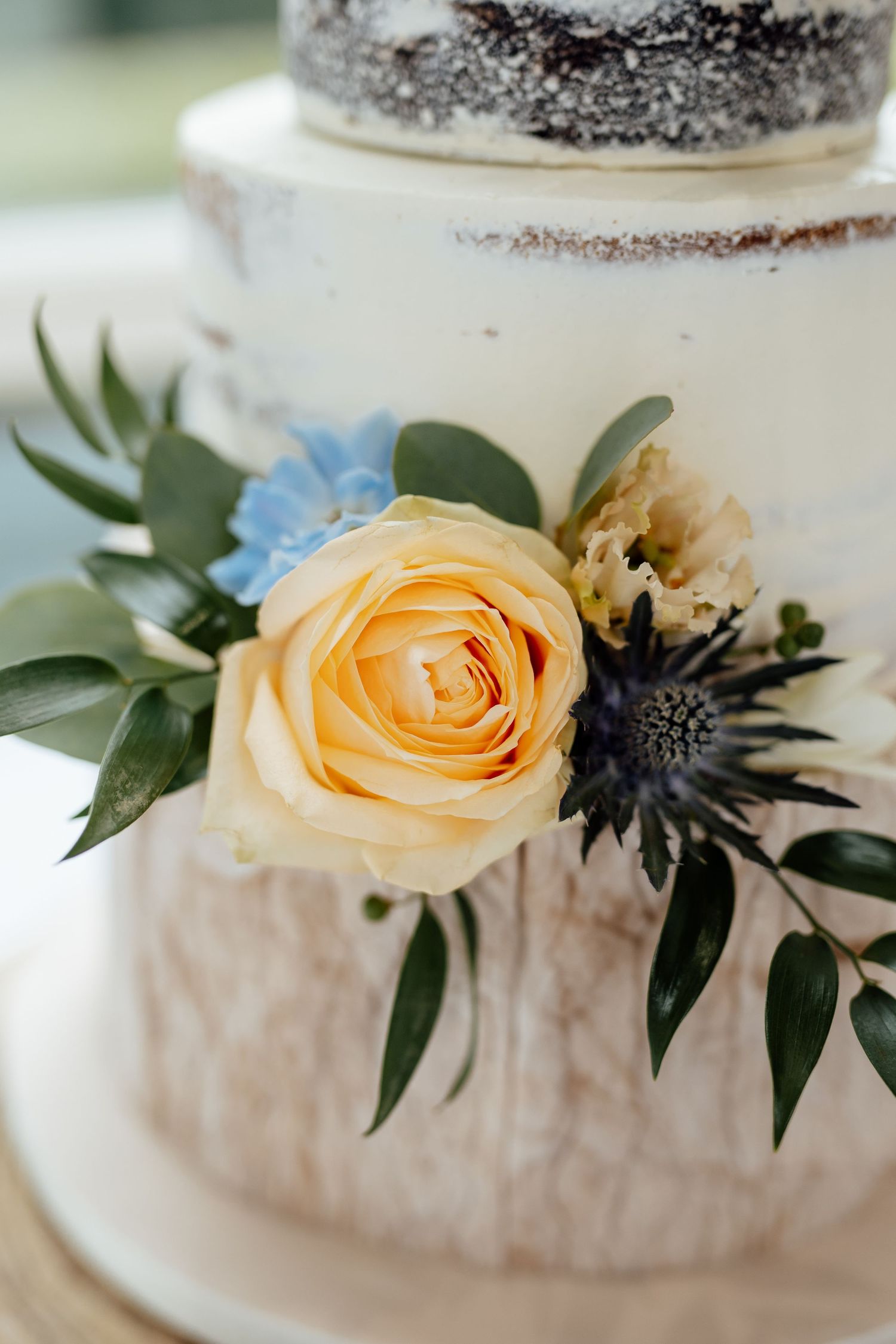 Elegant white wedding cake decorated with peach roses and greenery on display.