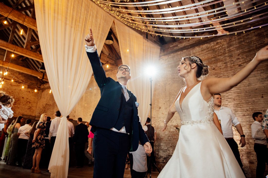 Couples dance under string lights and white draping at an elegant wedding reception.