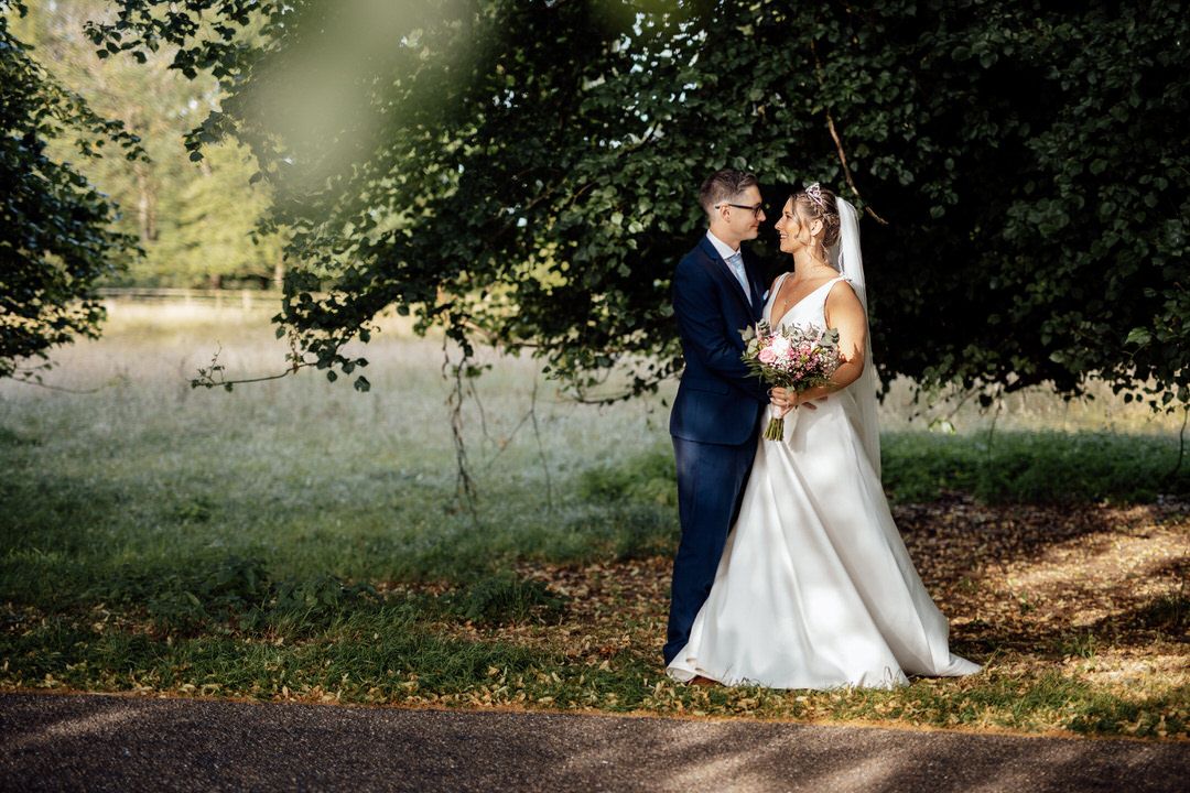 Couple poses for romantic wedding photos on tree-lined path.