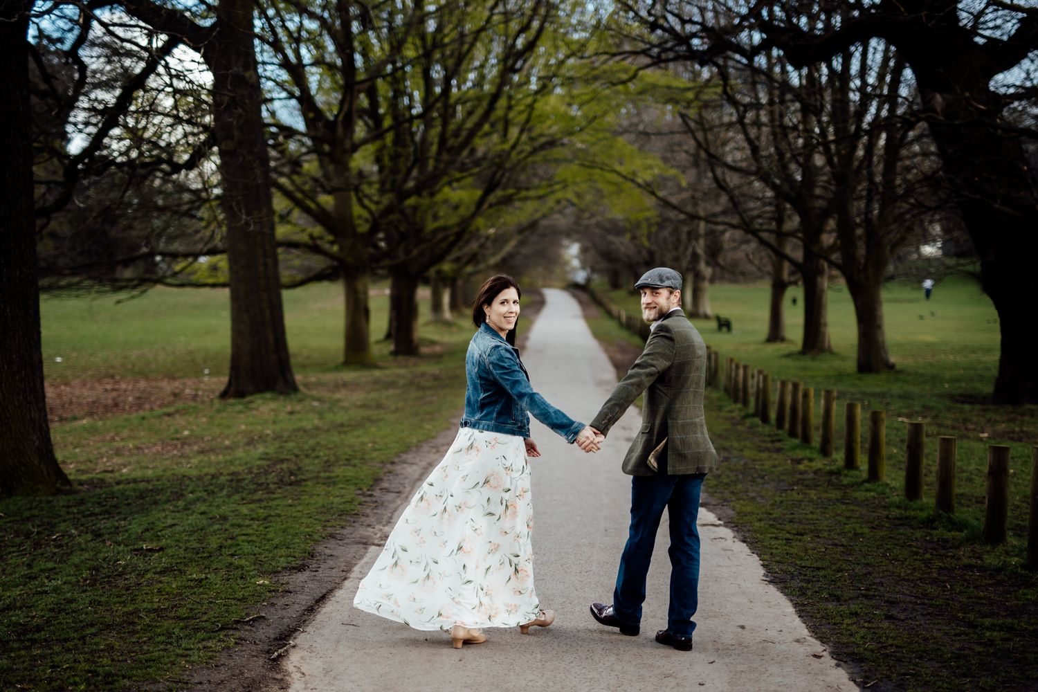 A couple walks along a tree-lined pathway in a scenic park setting.