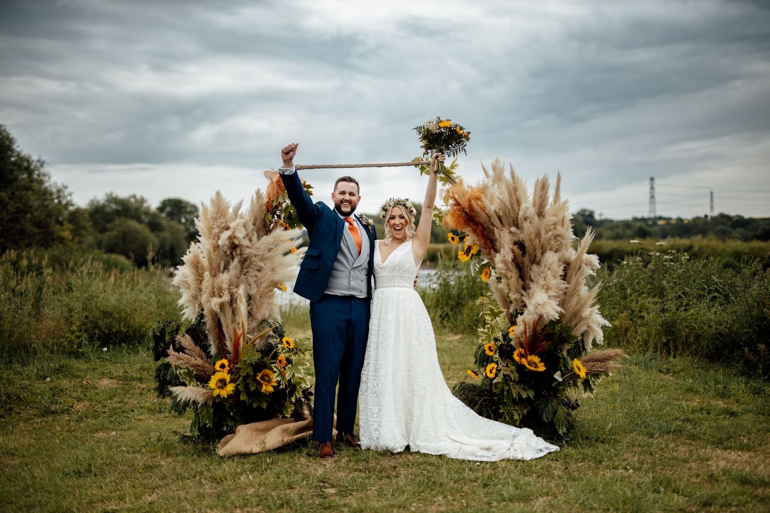 Newlyweds celebrating under floral arch with pampas grass and sunflowers.