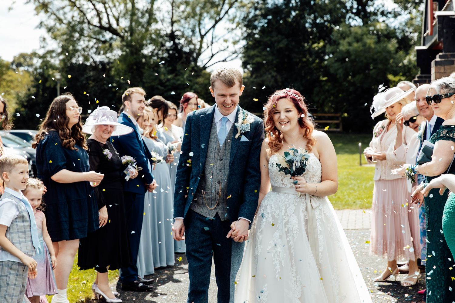 Wedding party and guests celebrate outdoors with confetti and joy.