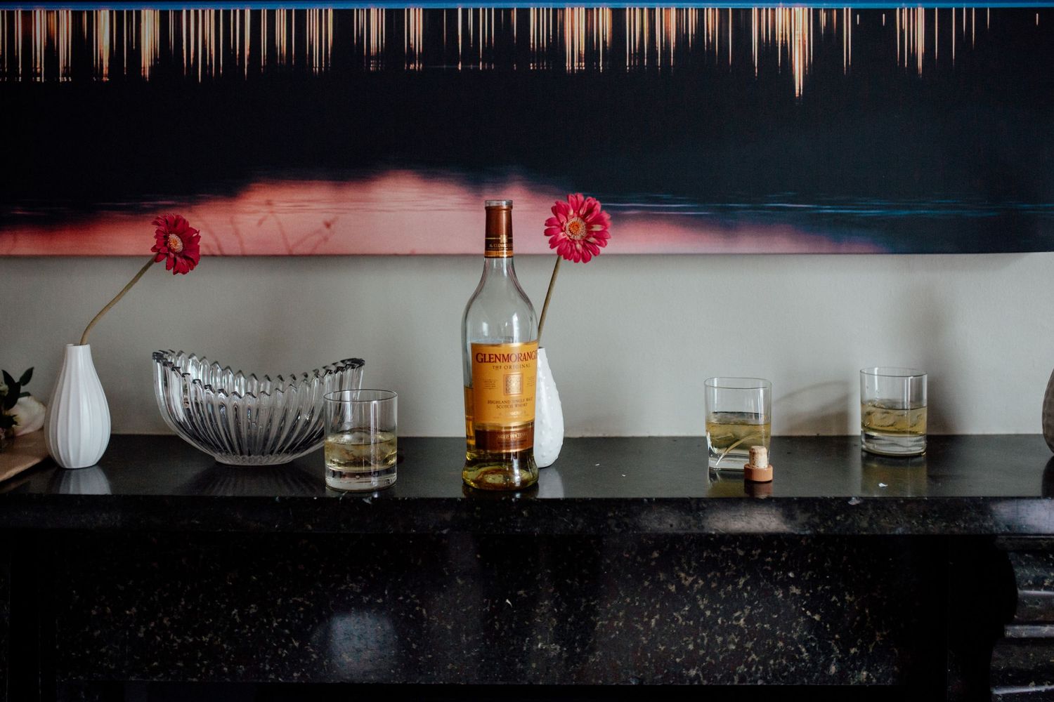 Row of whiskey glasses lined up on a dark bar counter with dramatic lighting.