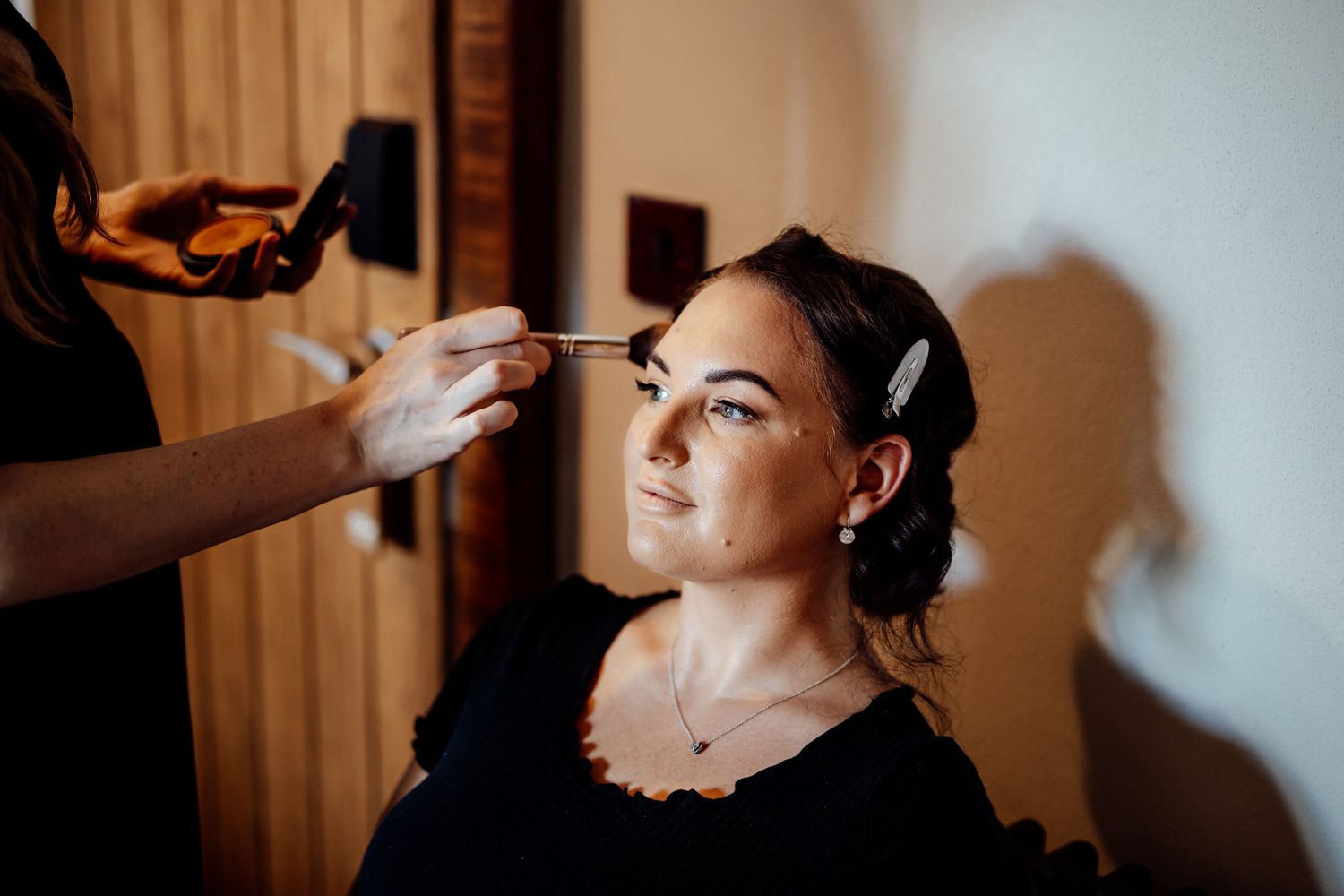 Makeup artist applying cosmetics in soft natural window light.