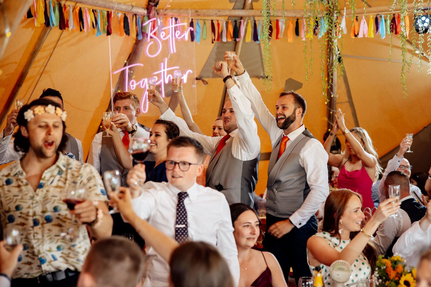 Wedding reception under orange tent with colorful tassel decorations and dancing guests.