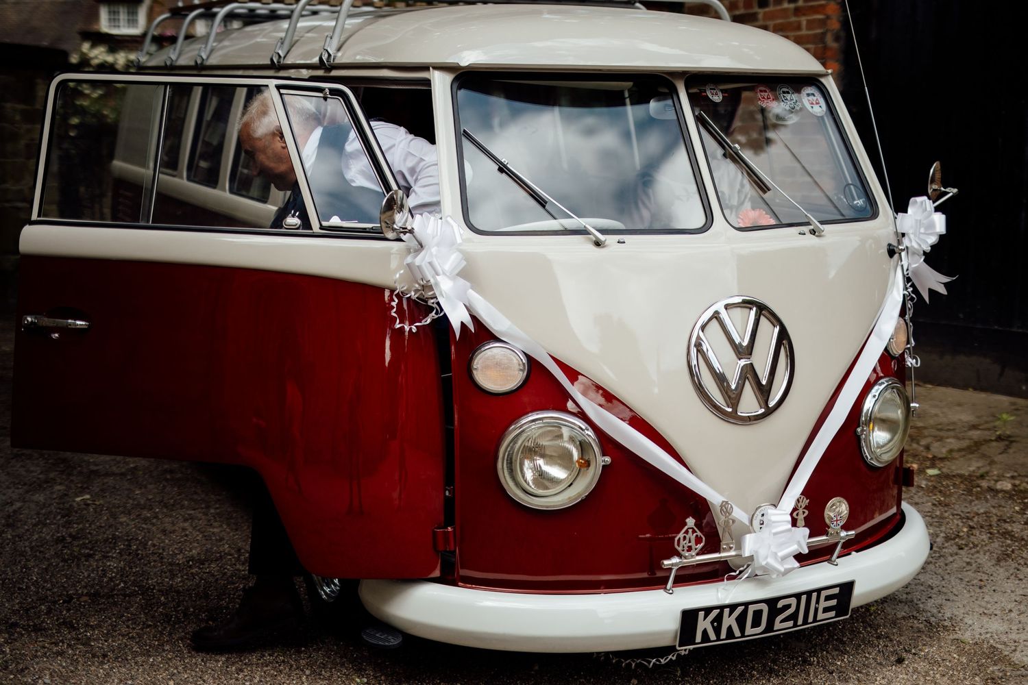 Classic red and white VW bus decorated with wedding ribbons parked outside.