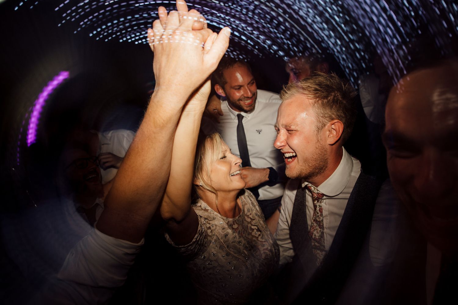 Guests dancing and celebrating on a dark dance floor with purple lighting.