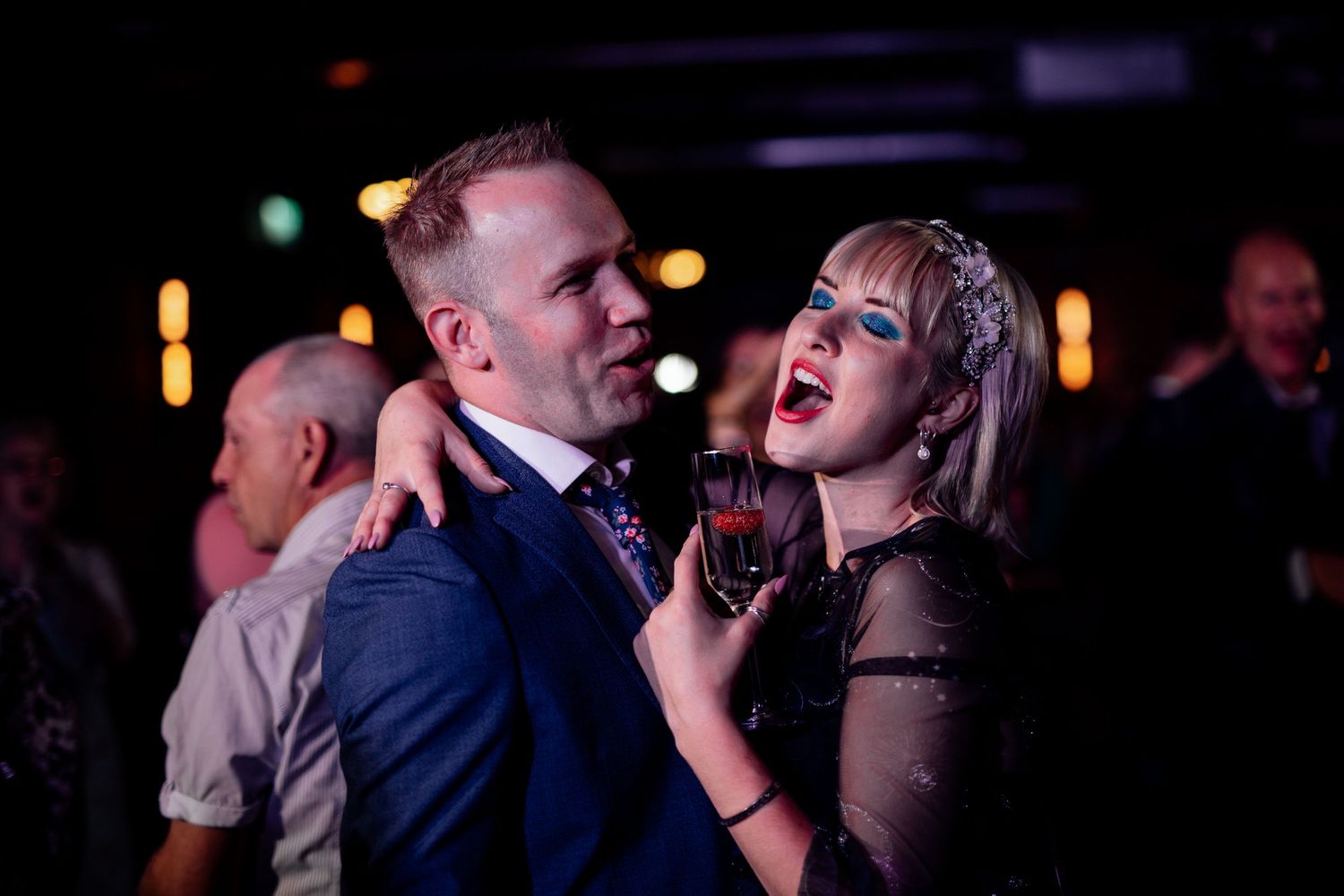 Wedding guests dancing and celebrating on a dimly lit dance floor during an evening reception.