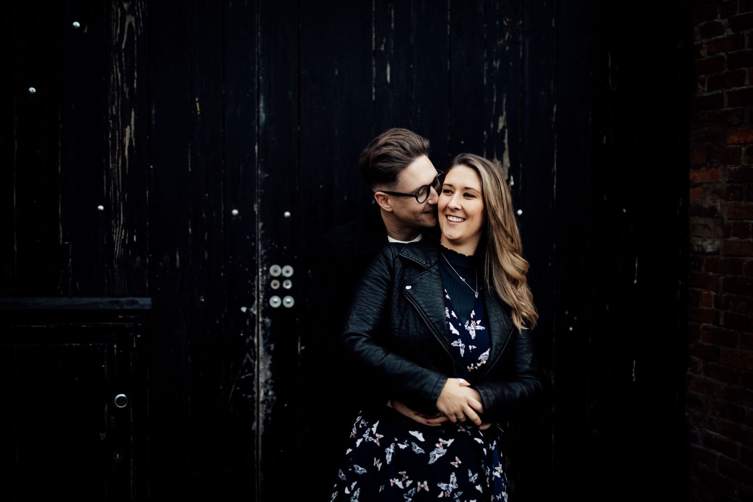 A romantic couple shares an intimate moment against a dark background in an artistic engagement photo.