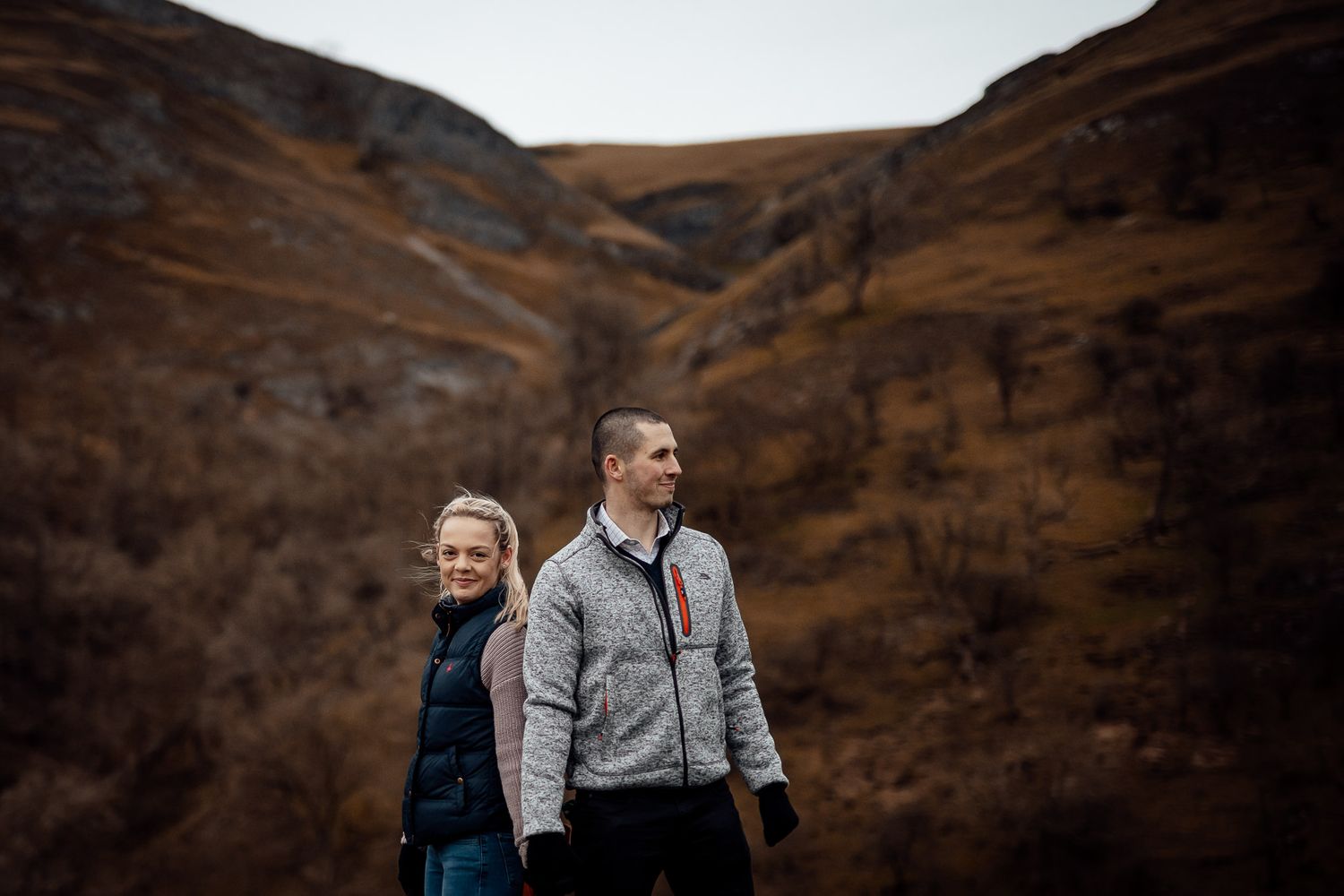 A couple explores rugged mountain terrain under moody autumn skies.
