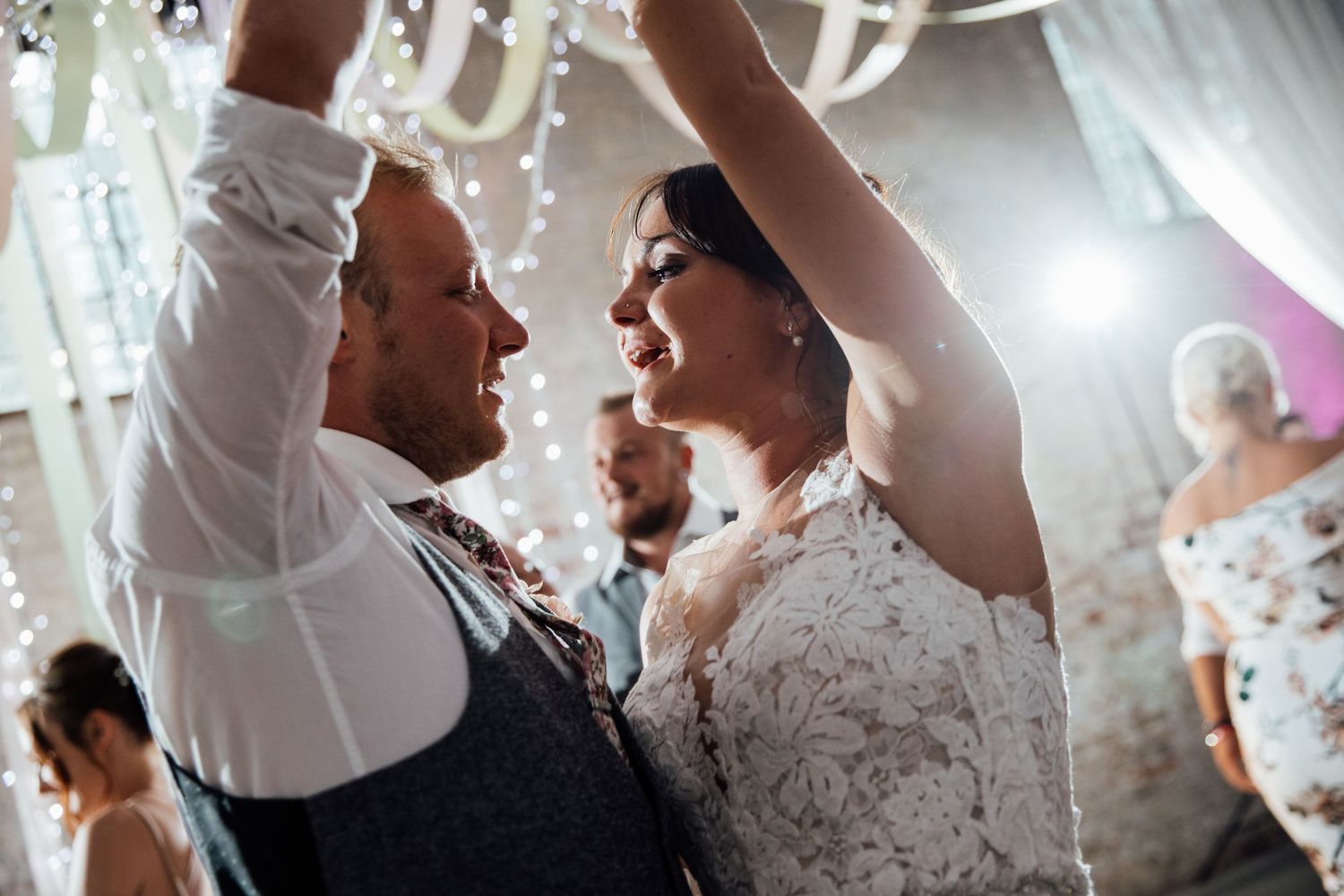 Joyful dancing and celebration during a wedding reception with white decor and lighting.