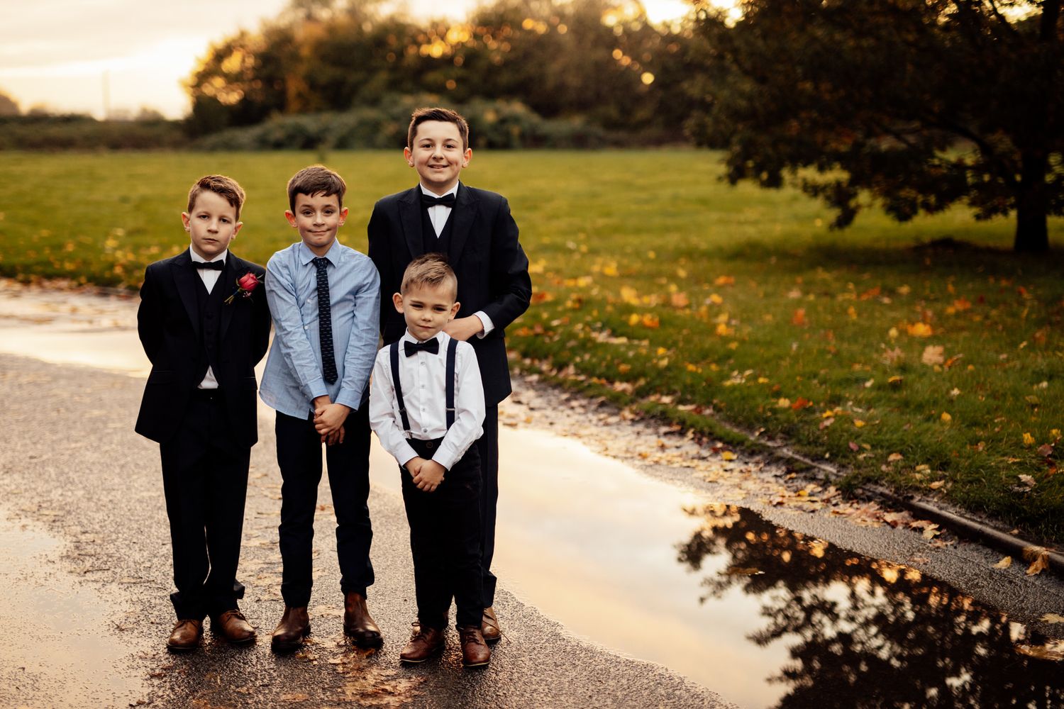 Young ring bearers in formal attire pose together on a garden path.