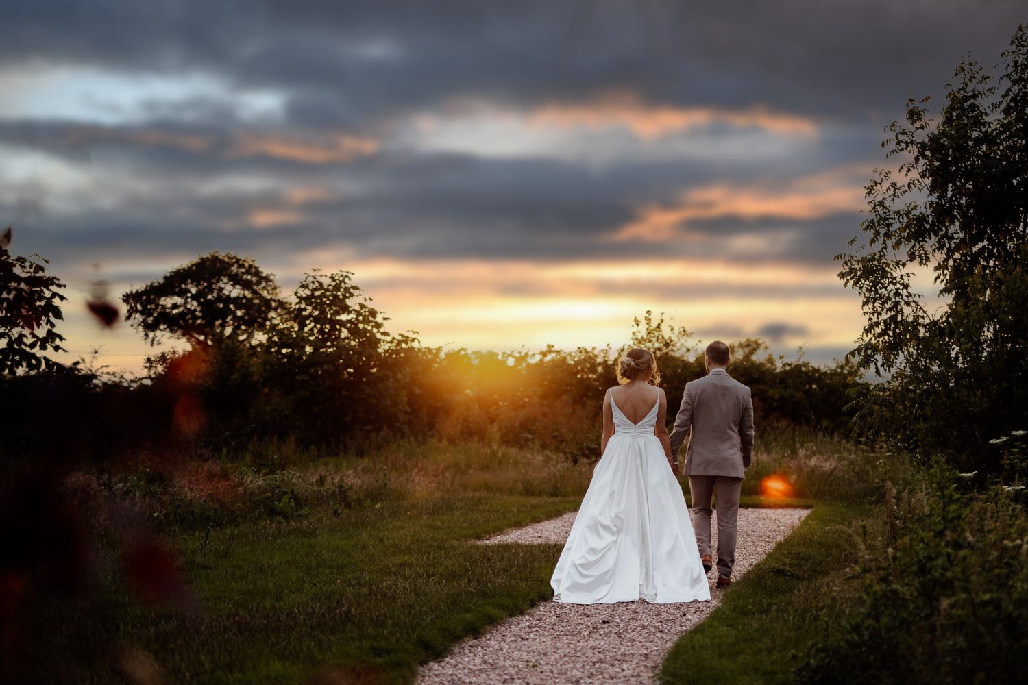 A dramatic sunset creates a golden glow behind a couple in a field.