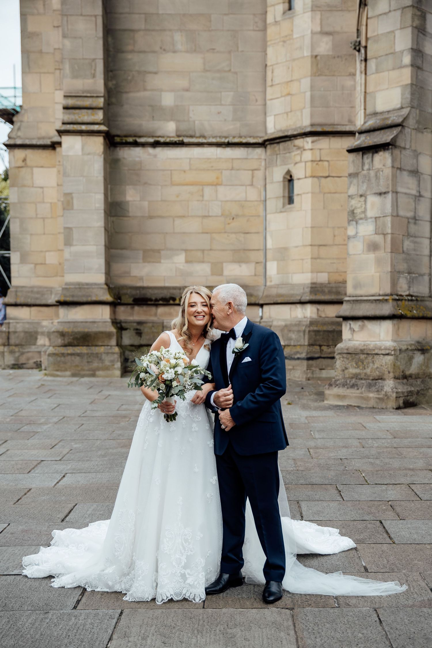 A couple poses for romantic wedding photos against a stone church exterior.