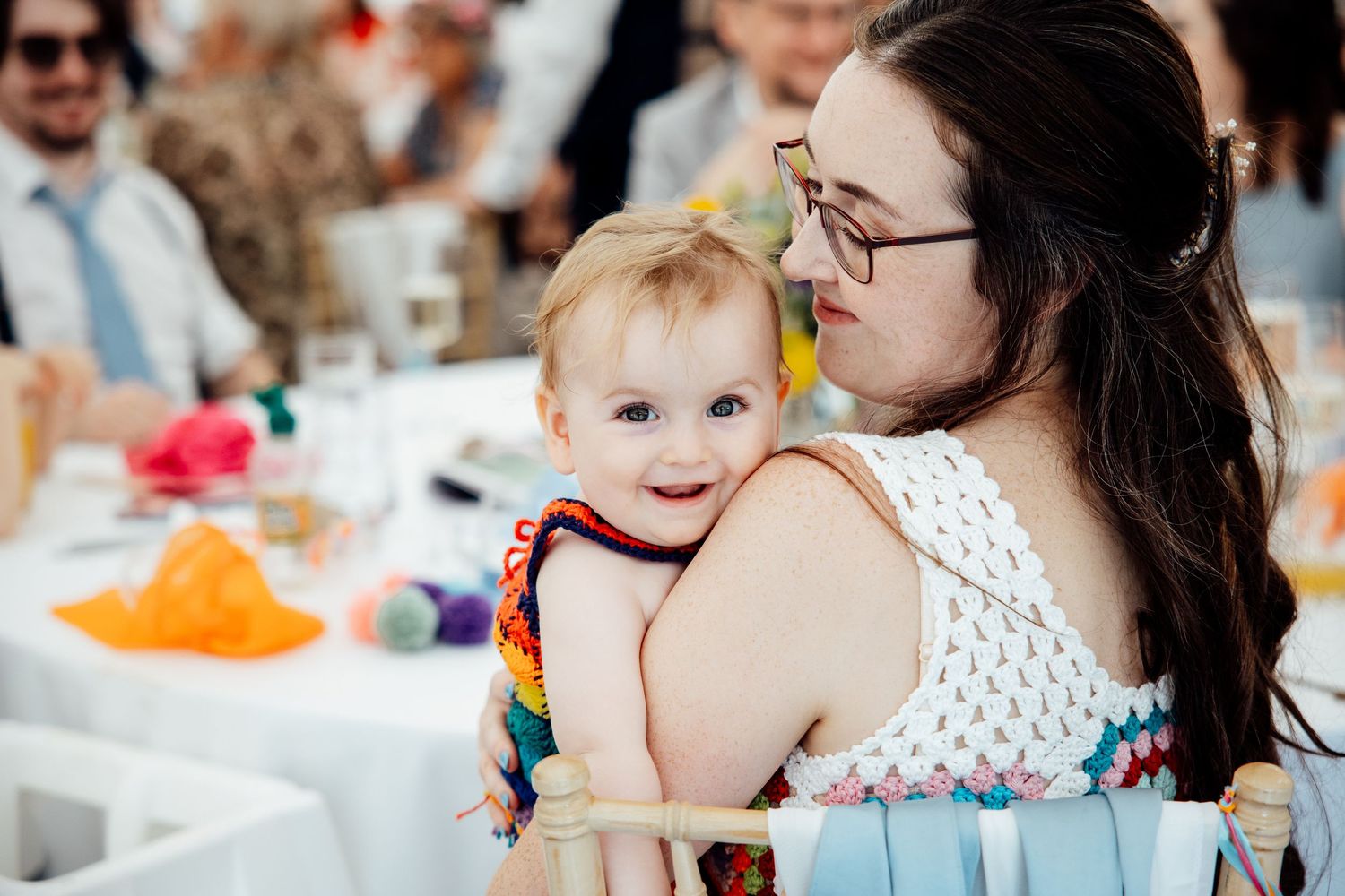A tender moment at a wedding reception with a baby wearing rainbow colors.