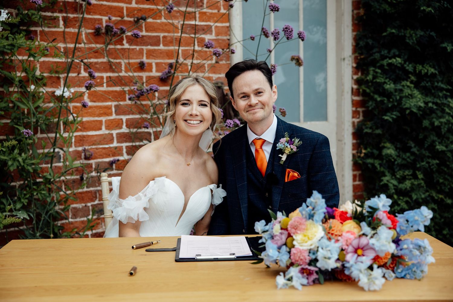 Rustic brick wall backdrop with floral arrangements at an outdoor wedding venue.