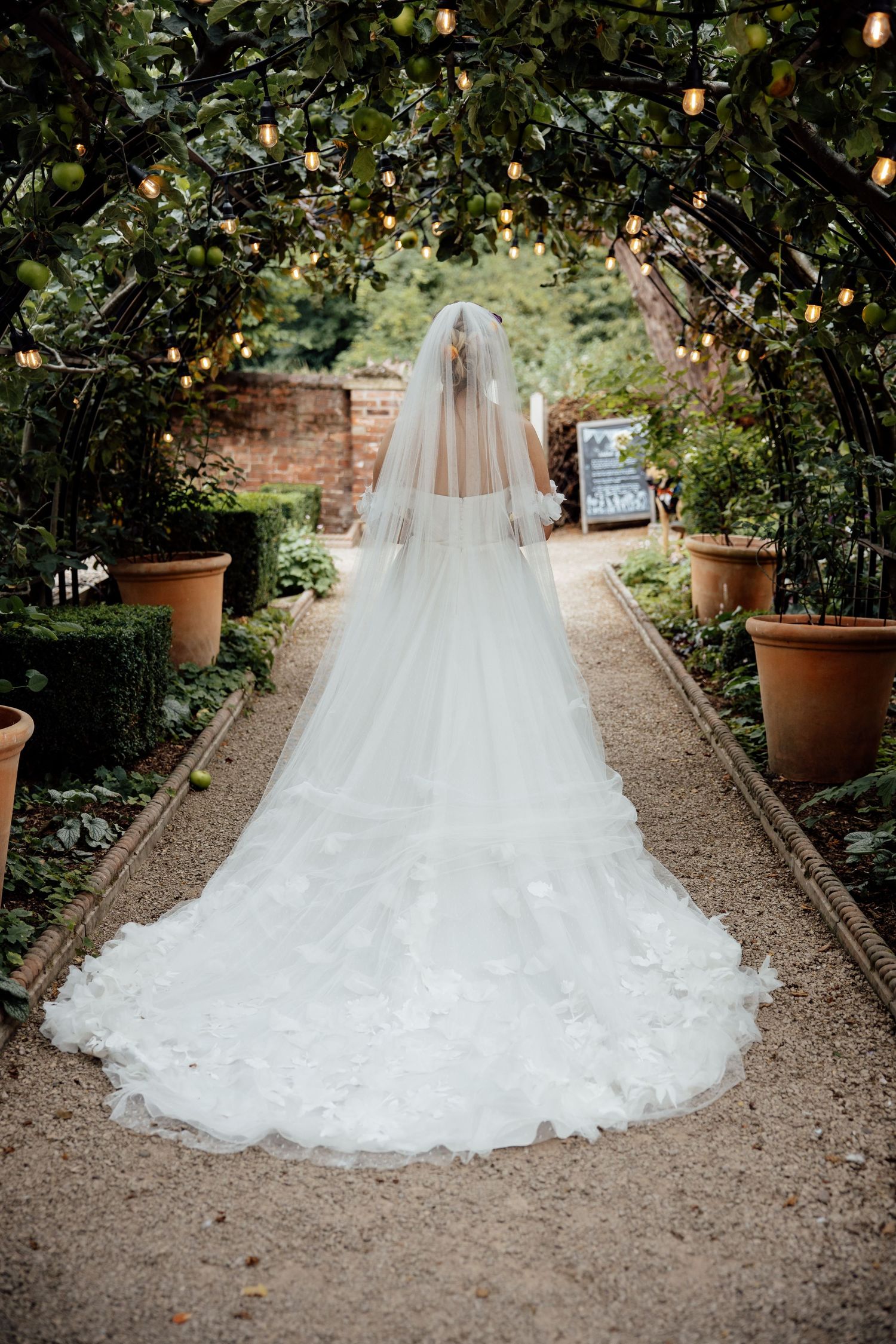 Stunning cathedral-length veil trailing down a garden path under string lights and greenery.