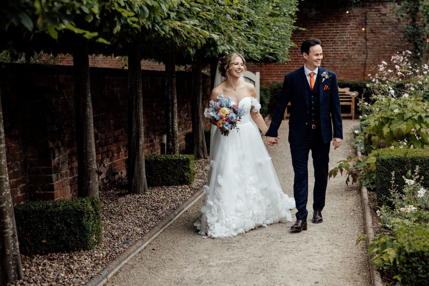 Garden wedding ceremony path lined with brick walls and greenery.