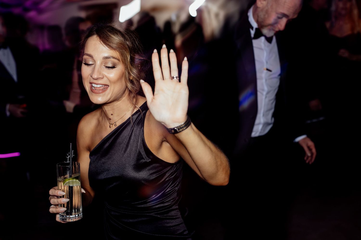 Wedding reception dance party with guests celebrating in formal attire under purple lighting.