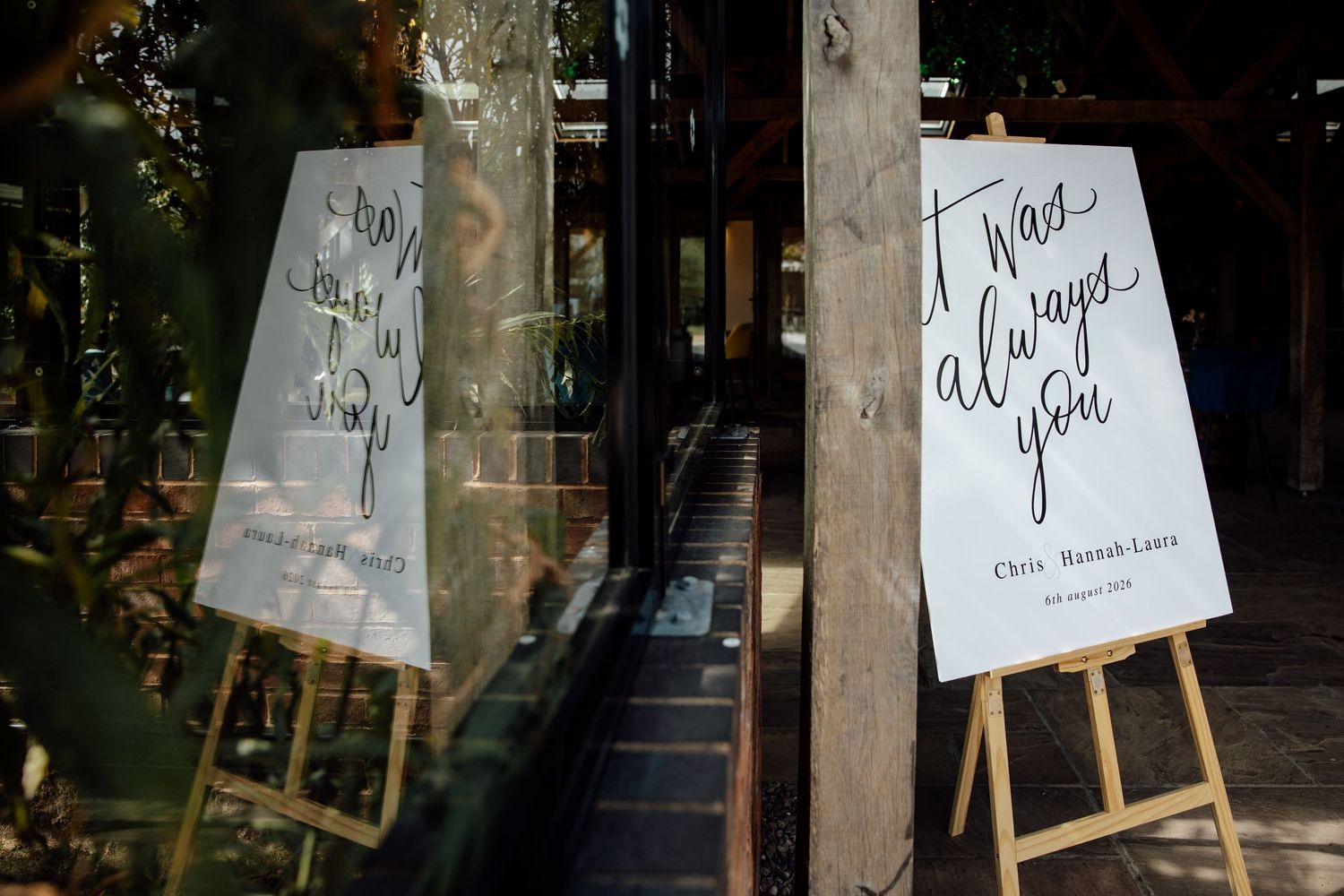 Two elegant calligraphy wedding signs on easels reading 'it was always you' displayed at venue entrance.