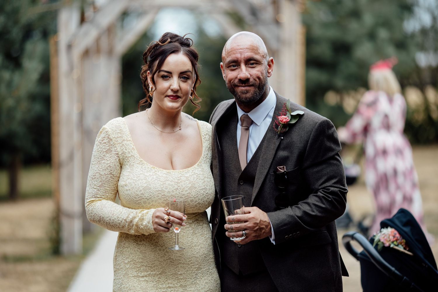 Newlywed couple smiling and holding champagne glasses outdoors at their wedding reception.