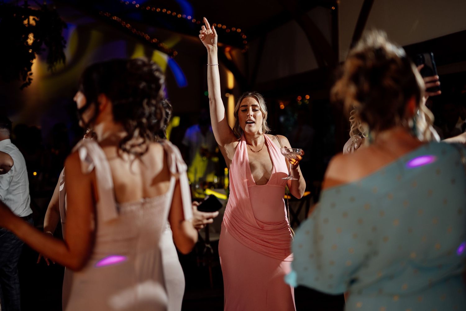 Wedding guest in pink dress dances energetically on the dance floor during evening wedding reception celebration.