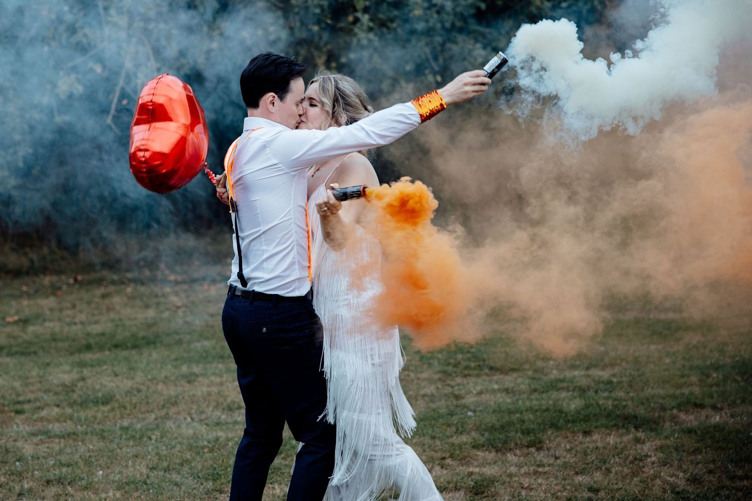Smoke bombs create dramatic orange effects during outdoor wedding photos.