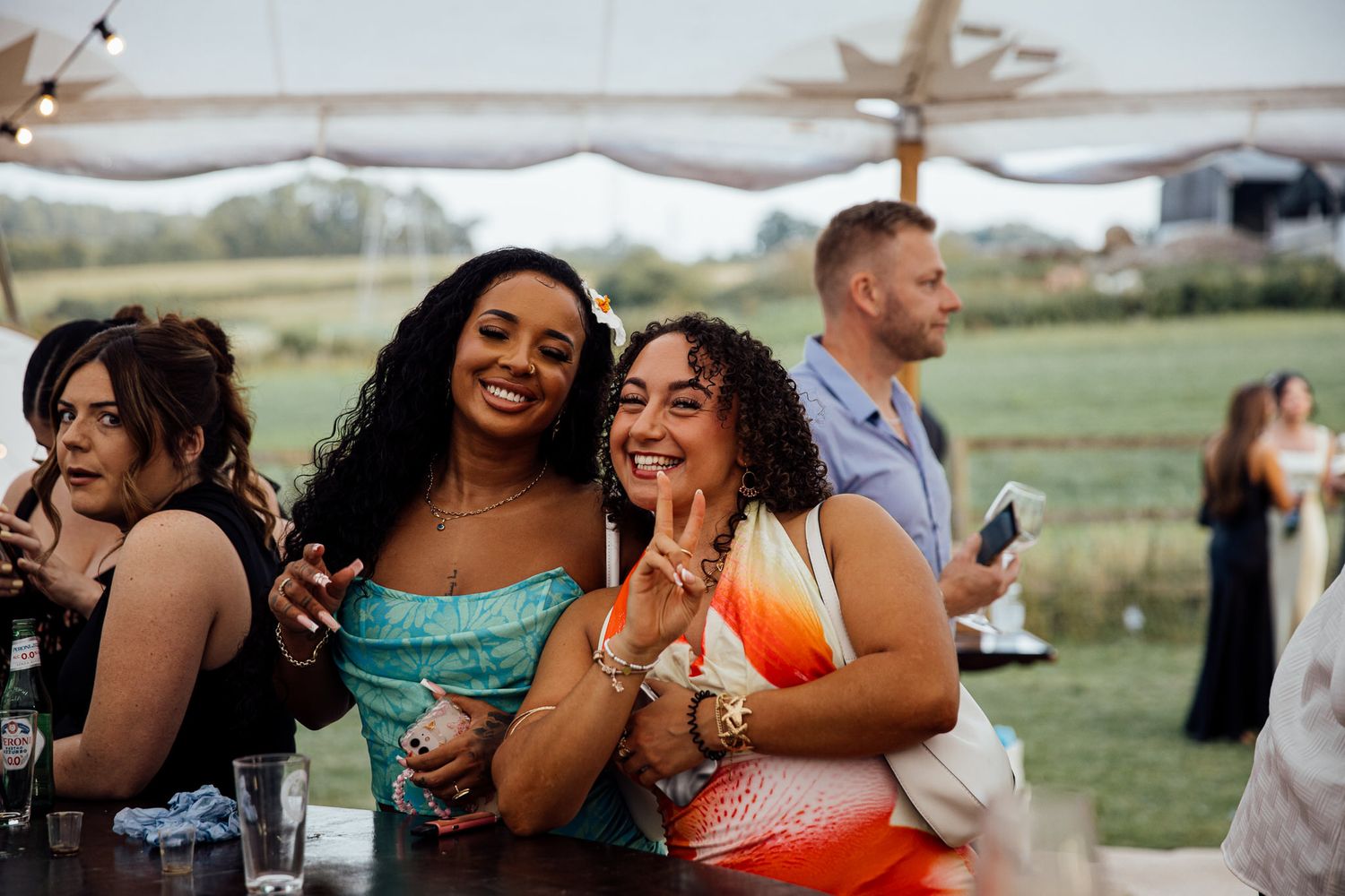 Wedding guests enjoying drinks and celebrating at outdoor reception under tent.