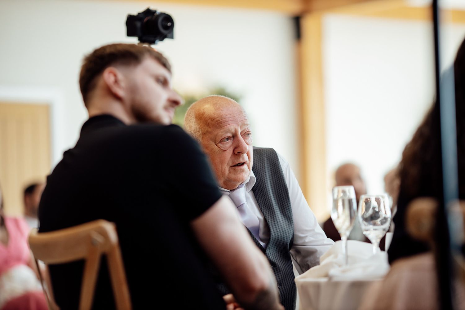 Wedding guests enjoying a reception dinner at elegantly set tables with wine glasses.