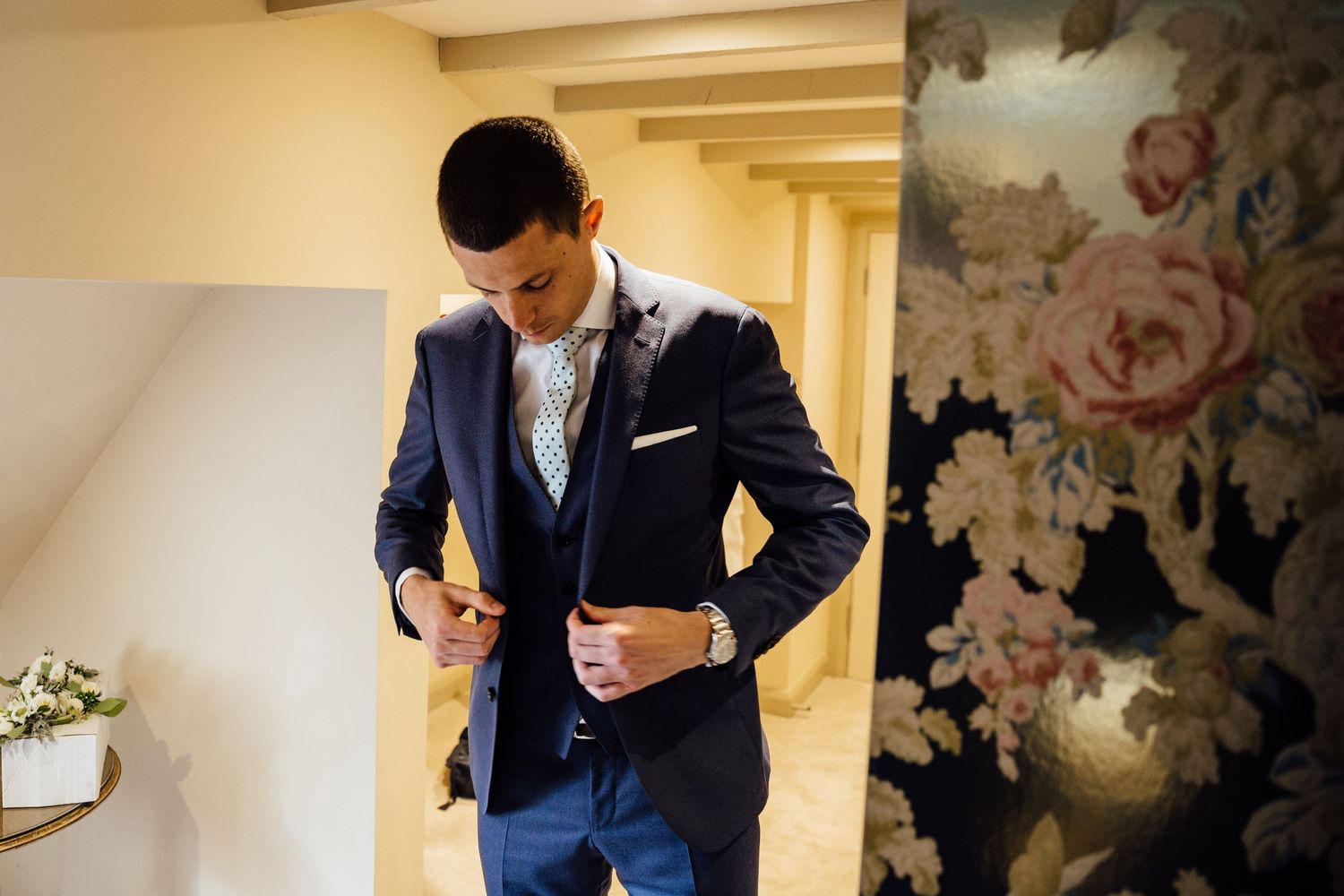 Wedding preparation scene in an elegant room with floral wallpaper and formal attire.