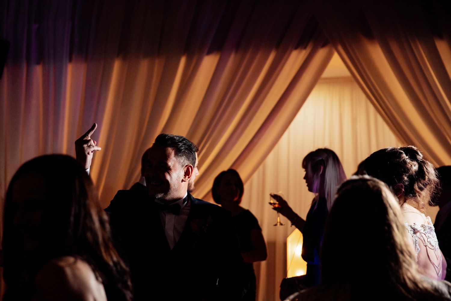 Silhouettes of wedding guests dancing at a dimly lit reception.