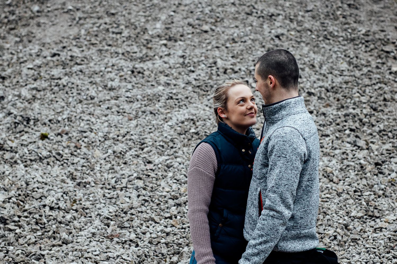 A couple embraces while standing on a rocky mountain path during an outdoor photoshoot.