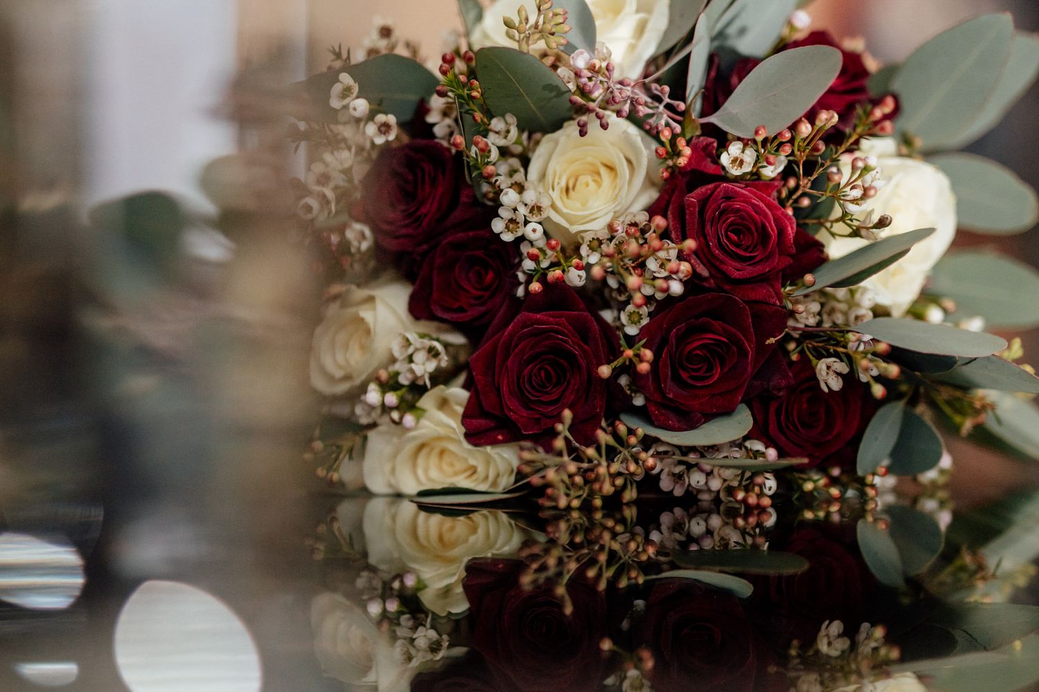 Wedding bouquet featuring deep red roses, white flowers and greenery with gold accents.
