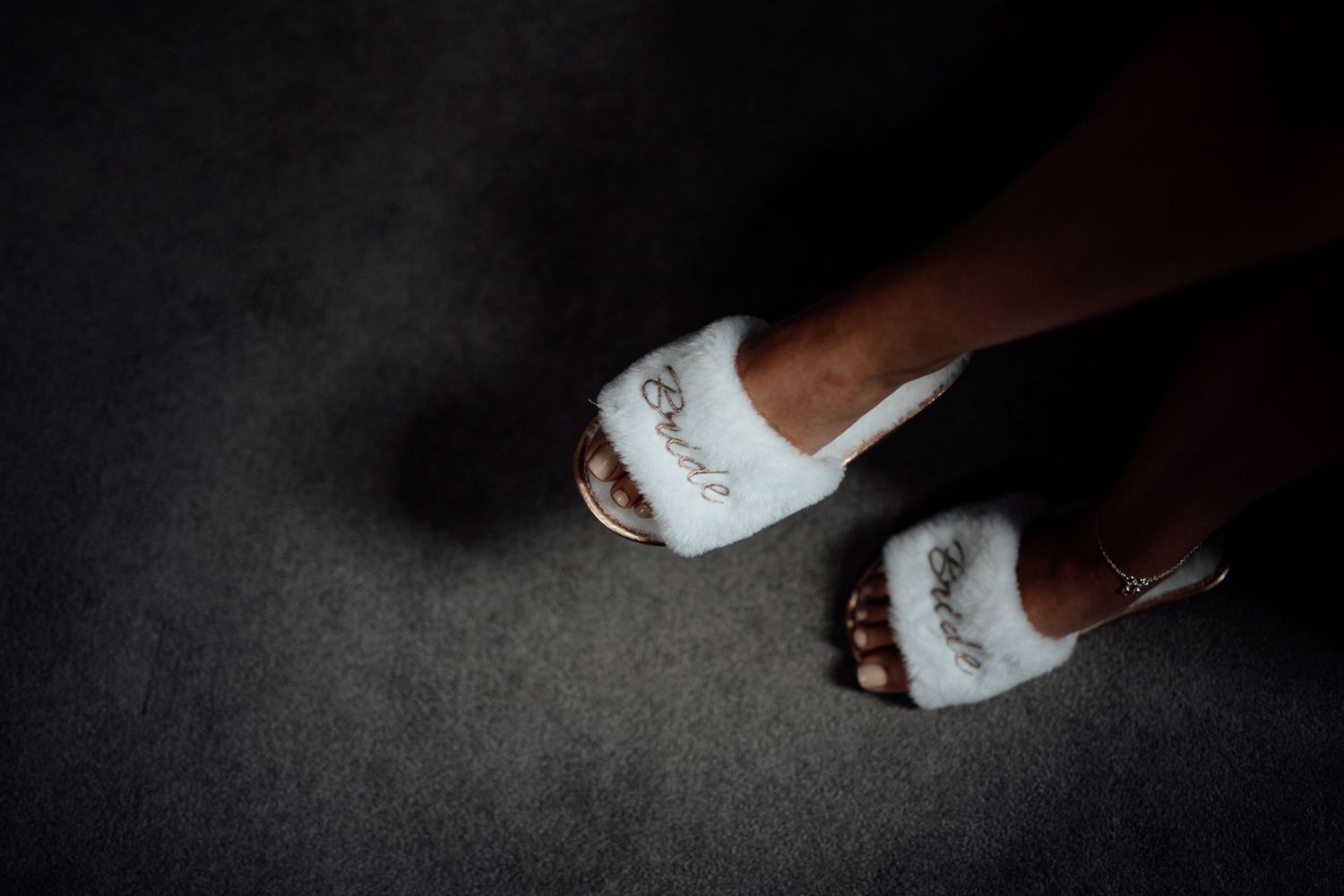 Close-up of white bridal shoes on dark flooring.