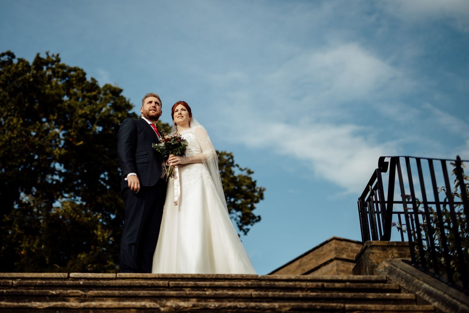Wedding couple photographed against blue sky on architectural steps.