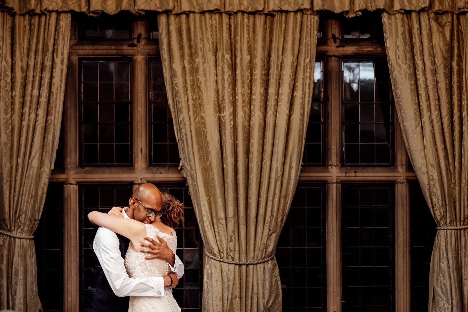 A tender embrace between two people by a window with elegant curtains.