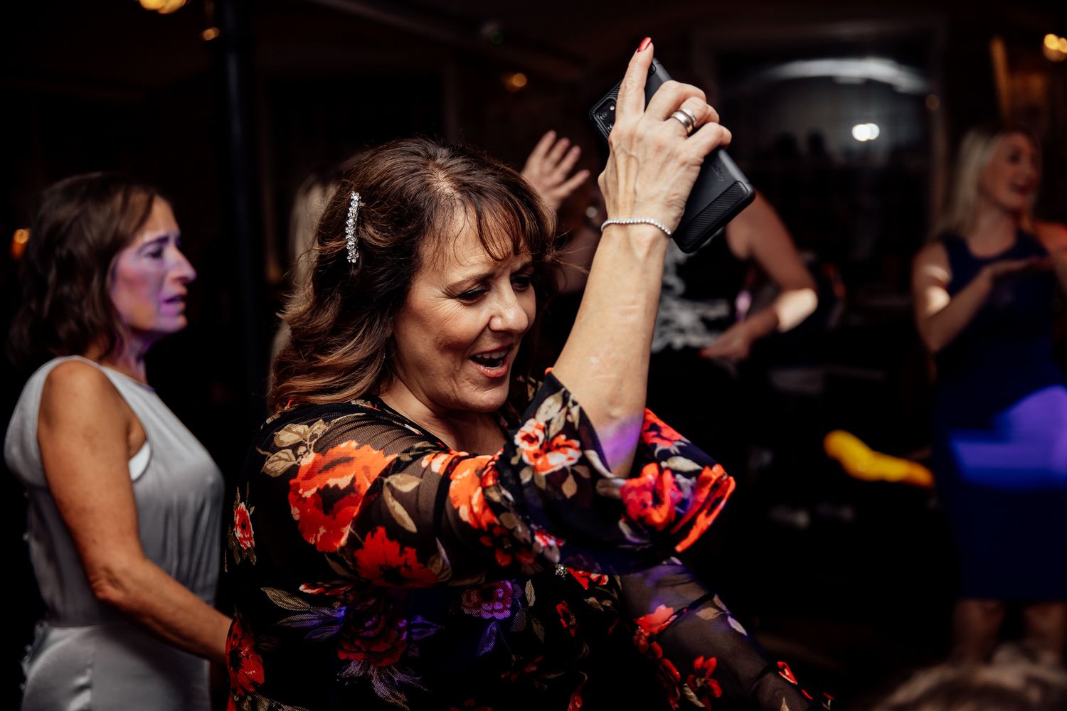 Wedding guests dancing and celebrating on a dark dance floor with colorful lighting.