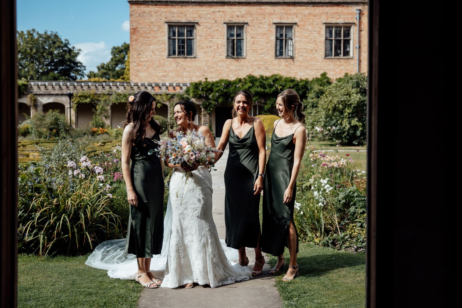 Wedding party posing for photos in a blooming garden outside a historic stone building.