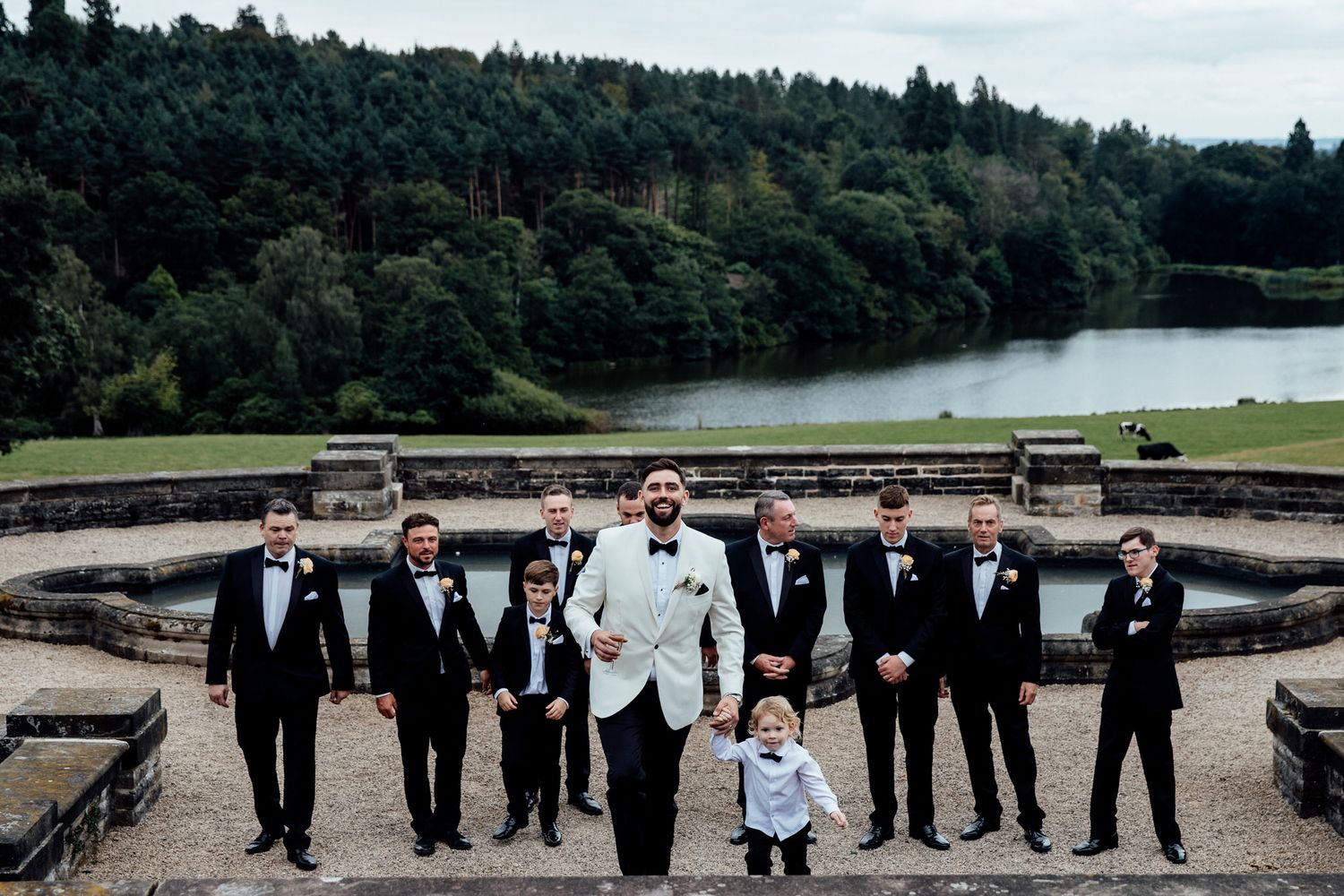 Wedding party poses along stone wall with scenic landscape view.