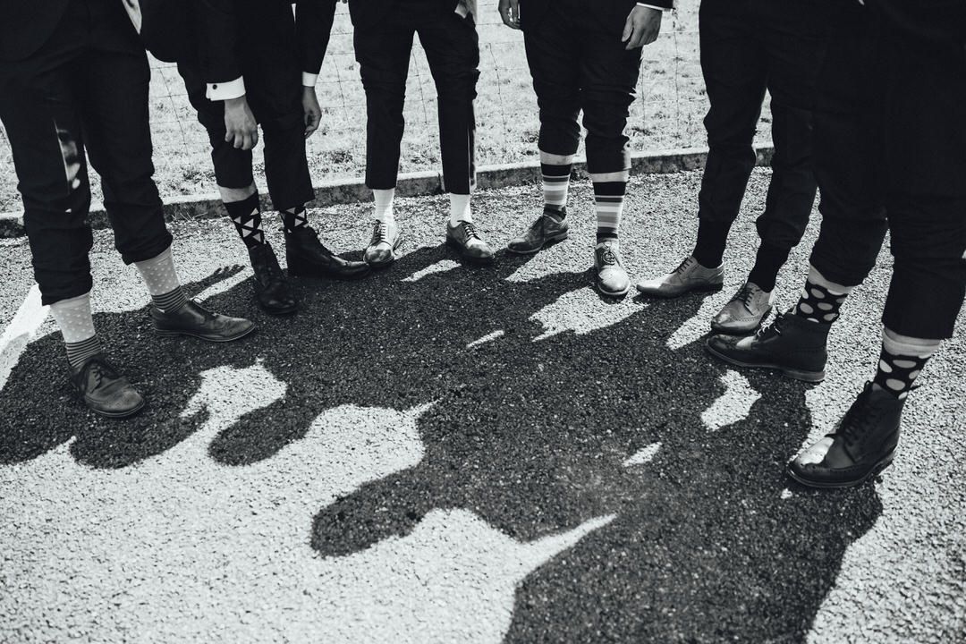 Black and white photo of groomsmen's feet and shadows lined up on pavement.