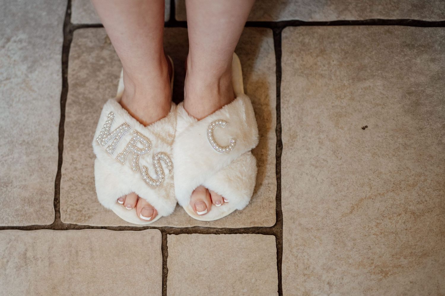 White bridal slippers with monogram detail on stone floor.