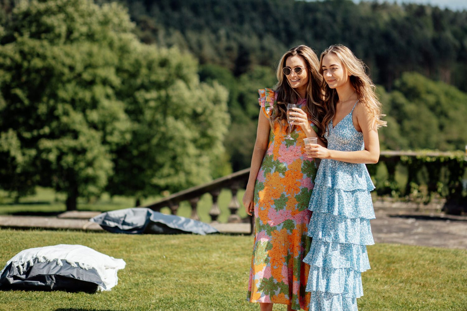 Wedding party members in colorful dresses and blue attire on sunny lawn.