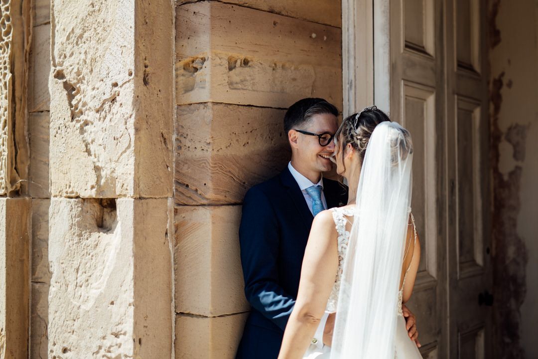 A couple shares a romantic moment under stone archways at a historic venue.
