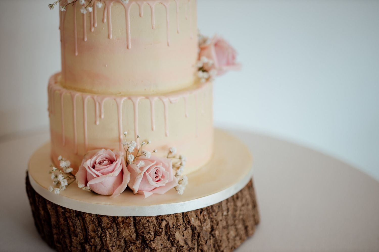 Elegant white wedding cake with pink drip details and floral decorations on a rustic wood base.
