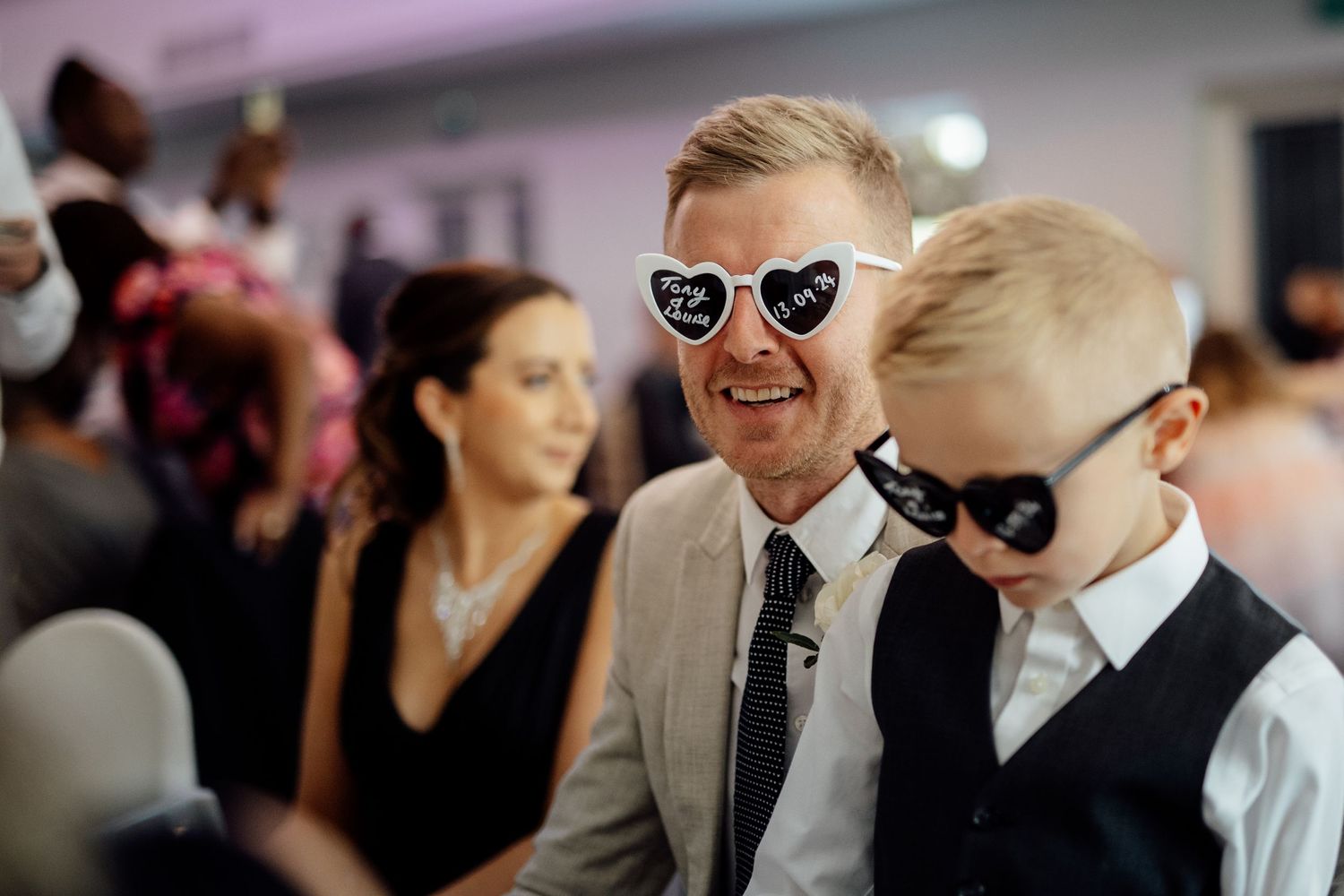 Wedding guests wearing sunglasses smile and laugh during outdoor celebration.